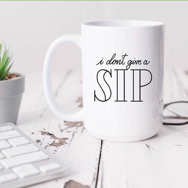 15oz white ceramic mug with hand lettered illustrated design that says I don't give a sip shown sitting on a white office desk