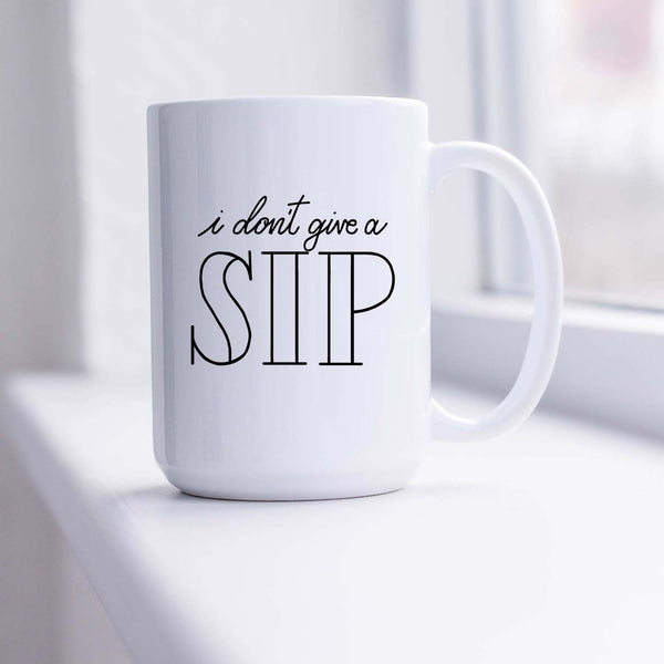 15oz white ceramic mug with hand lettered illustrated design that says I don't give a sip shown in a sunny window