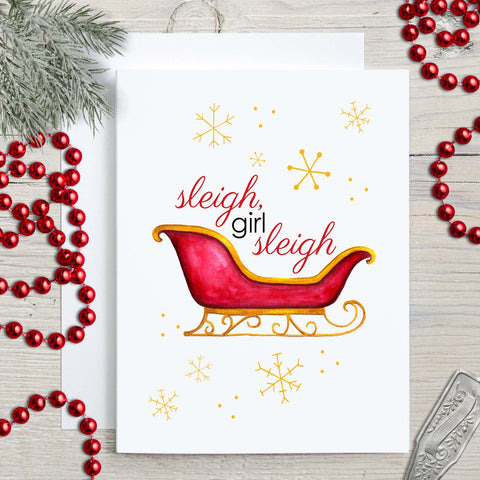Watercolor Christmas greeting card with a watercolor painted red and gold sleigh and gold snowflakes with message that says sleigh, girl sleigh shown with holiday decorations