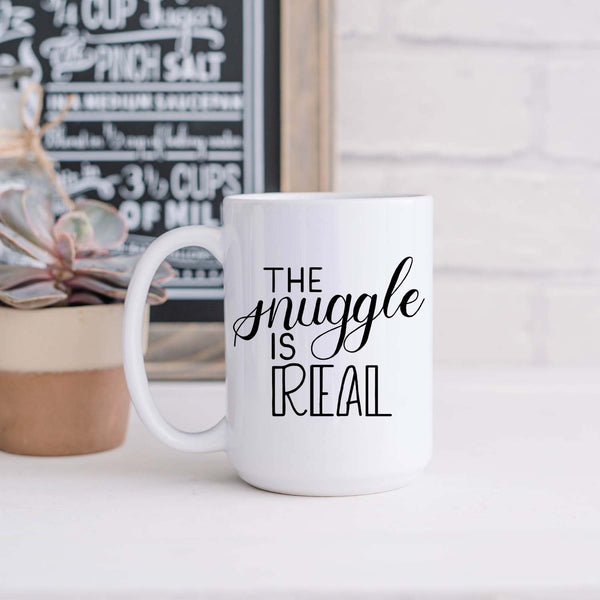15oz white ceramic mug with hand lettered illustrated design that says the snuggle is real shown sitting in a kitchen