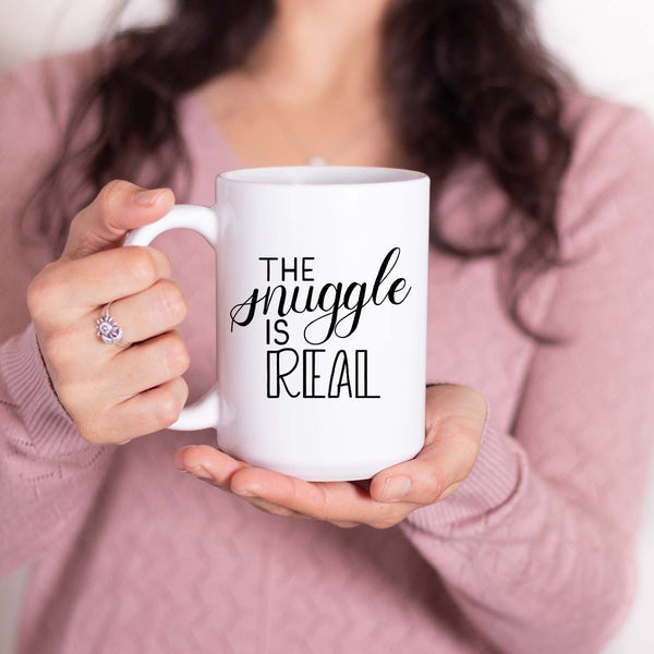 15oz white ceramic mug with hand lettered illustrated design that says the snuggle is real shown with a woman holding the mug