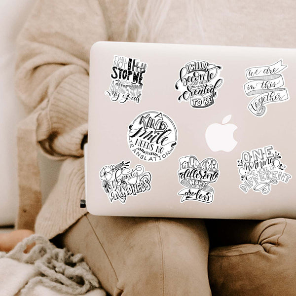 Collection of inspirational and motivational black and white  stickers  shown on a MacBook cover sitting open on a woman's lap