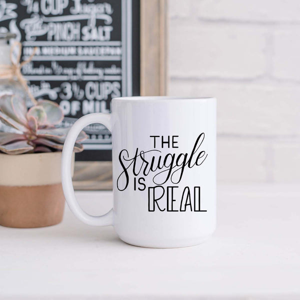 15oz white ceramic mug with hand lettered illustrated design that says the struggle is real shown sitting in a kitchen