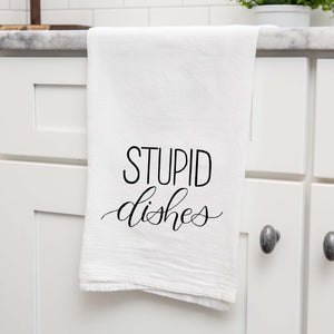 White floursack towel with black hand lettered illustrated design that says Stupid dishes shown folded and hanging from a countertop in a modern kitchen