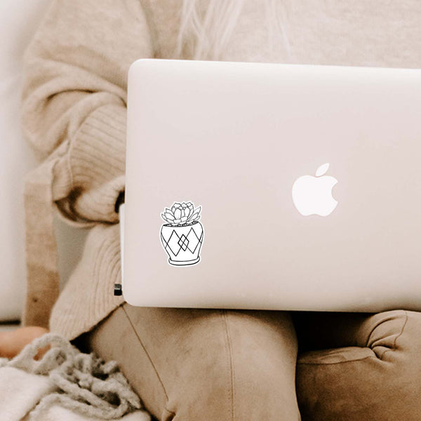 3" black and white hand illustration of a succulent plant in a mini pot shown adhered to a MacBook laptop cover sitting open on a woman's lap