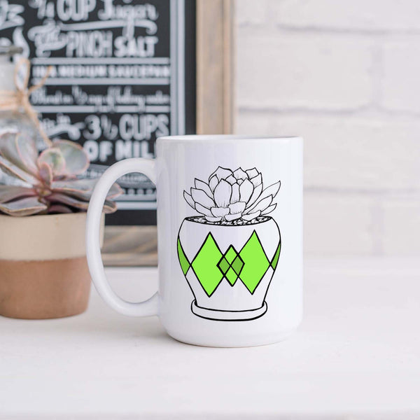 15oz white ceramic mug with hand lettered illustrated design of a succulent plant in a pot with green diamond pattern shown sitting in a kitchen