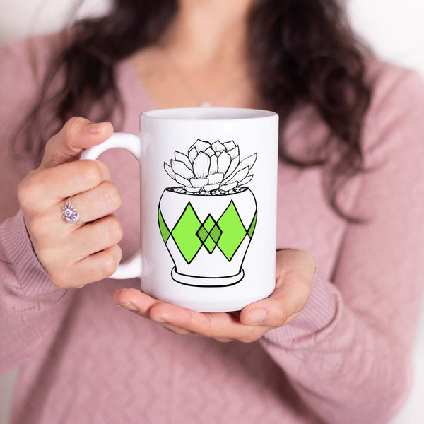 15oz white ceramic mug with hand lettered illustrated design of a succulent plant in a pot with green diamond pattern shown with a woman holding the mug