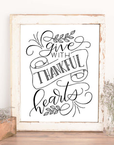 wall art design that says give with thankful hearts in hand lettering and calliagraphy with illustrated swirls, leaves and ribbon banner in black and white