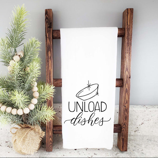 White floursack towel with black hand lettered illustrated design that says Unload dishes with a clean bowl doodle shown folded and hanging from a wooden display ladder and mini Christmas tree