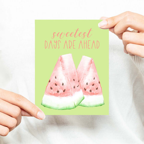 watercolor pink and green watermelon slices on a greeting card that says sweetest days are ahead with a white A2 envelope shown with a woman in a white sweater holding card
