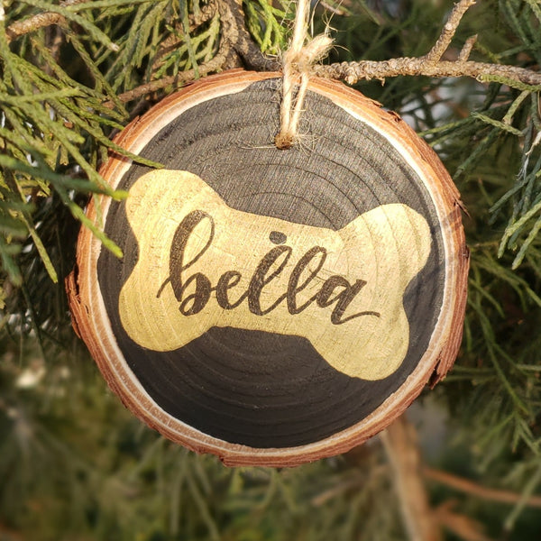 rustic wood slice ornament with hand drawn dog bone with pet name inside in black hand lettering hanging in a tree