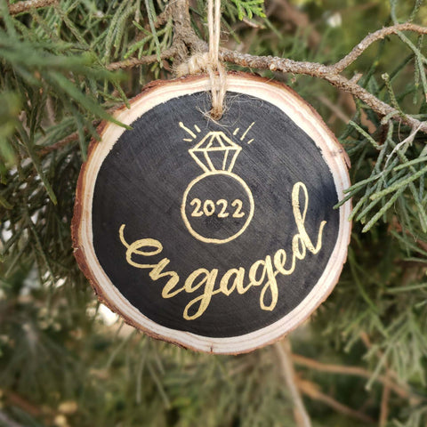 Hand painted rustic wood slice ornament that says engaged with the year and a diamond ring illustration doodle
