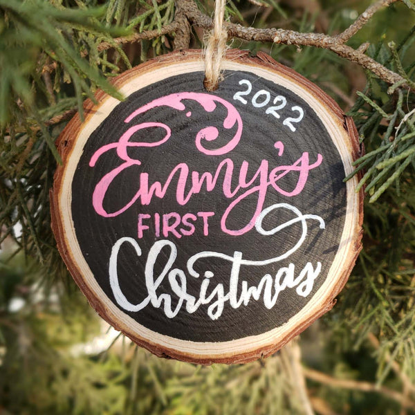Hand painted rustic wood slice ornament personalized with baby's first name and the year and says first christmas in hand lettering
