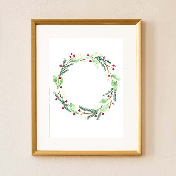 Watercolor painted holiday wreath with greens, branches and red berries shown hanging on a wall in a gold frame with a white mat.