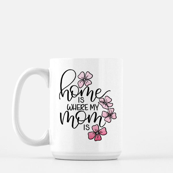 15oz white ceramic mug with hand lettered illustrated design that says home is where my mom is with pink flower illustrations