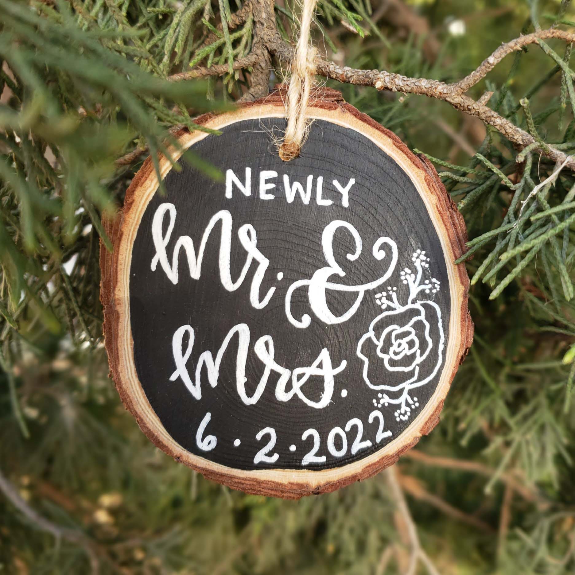Hand painted rustic wood slice ornament that says newly mr & mrs with wedding date in hand lettering and sweet floral doodle accents