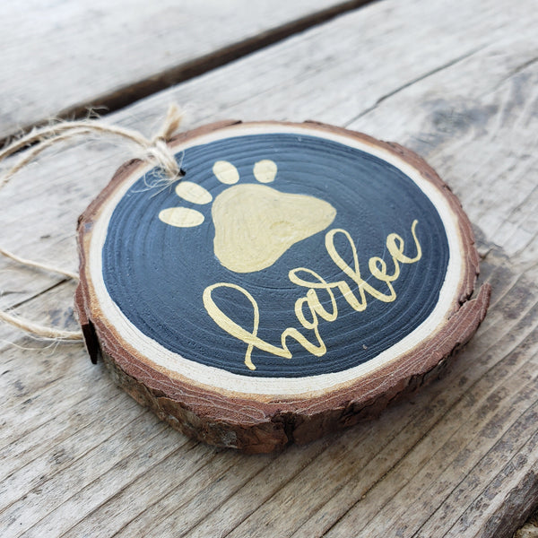 rustic wood slice ornament that says your pet's name hand lettered in gold with a paw print in gold