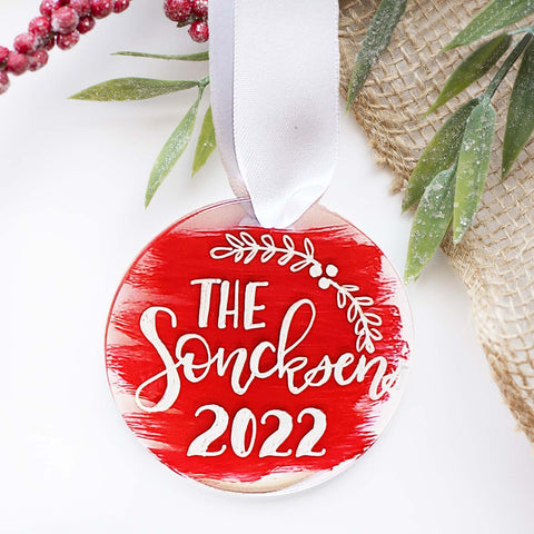 Custom Round clear acrylic ornament personalized with own message and year in hand lettering with a white silk ribbon and red paint strokes on the background